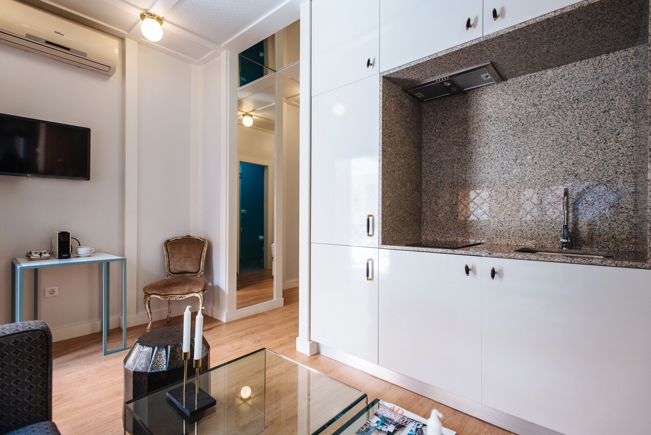 Una cocina moderna con armarios blancos, encimera de granito y estufa integrada. En primer plano, una pequeña mesa con cubierta de vidrio y una silla.
