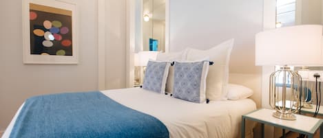 A neatly arranged bedroom with a bed, pillows, a bedside table, and a mirror.