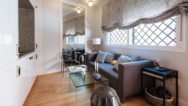 Un salon moderne avec une table basse en verre, un canapé agrémenté de coussins à motifs et une grande fenêtre ornée de rideaux à motifs.