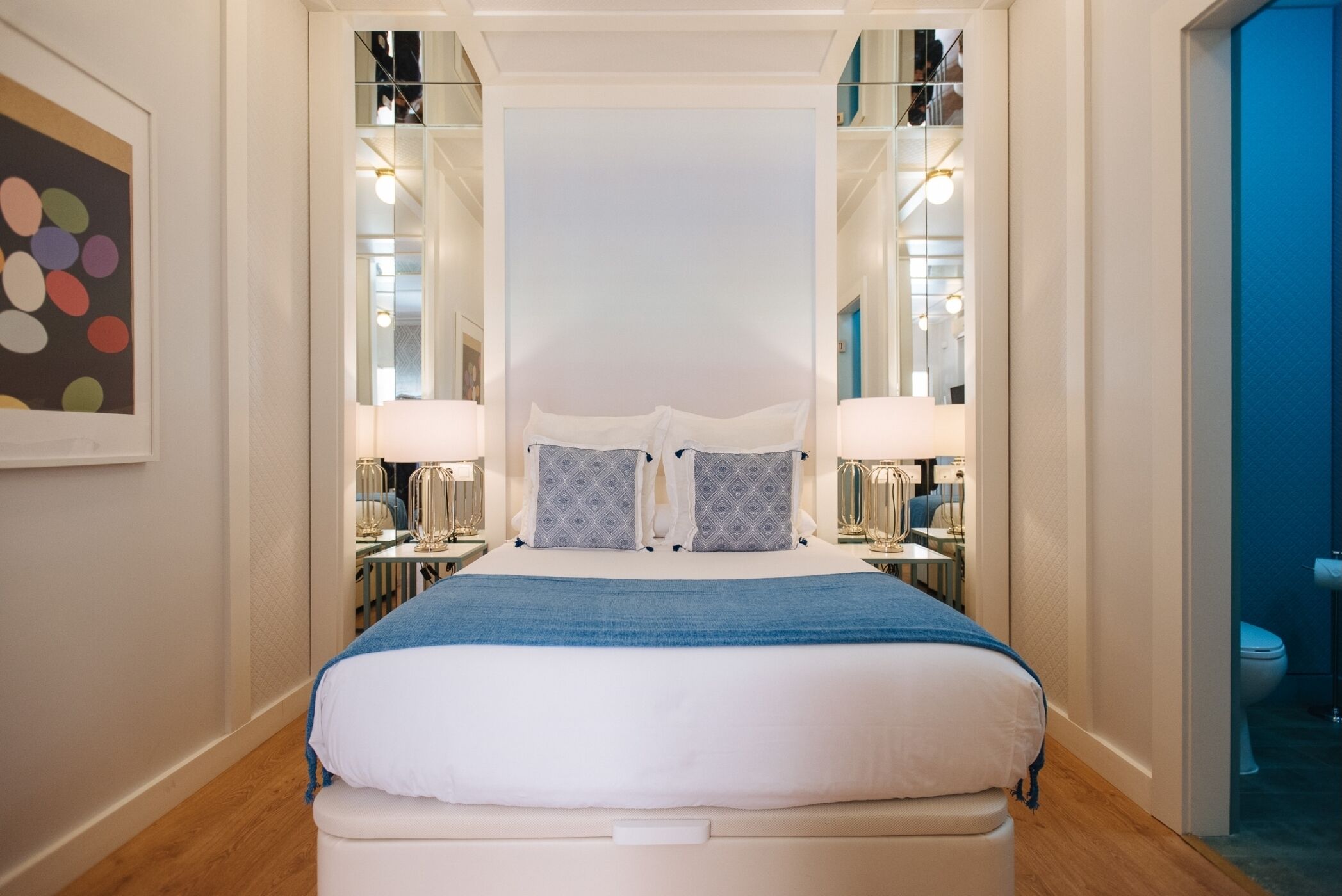 A neatly arranged bedroom with a large bed, bedside lamps, and a mirror.