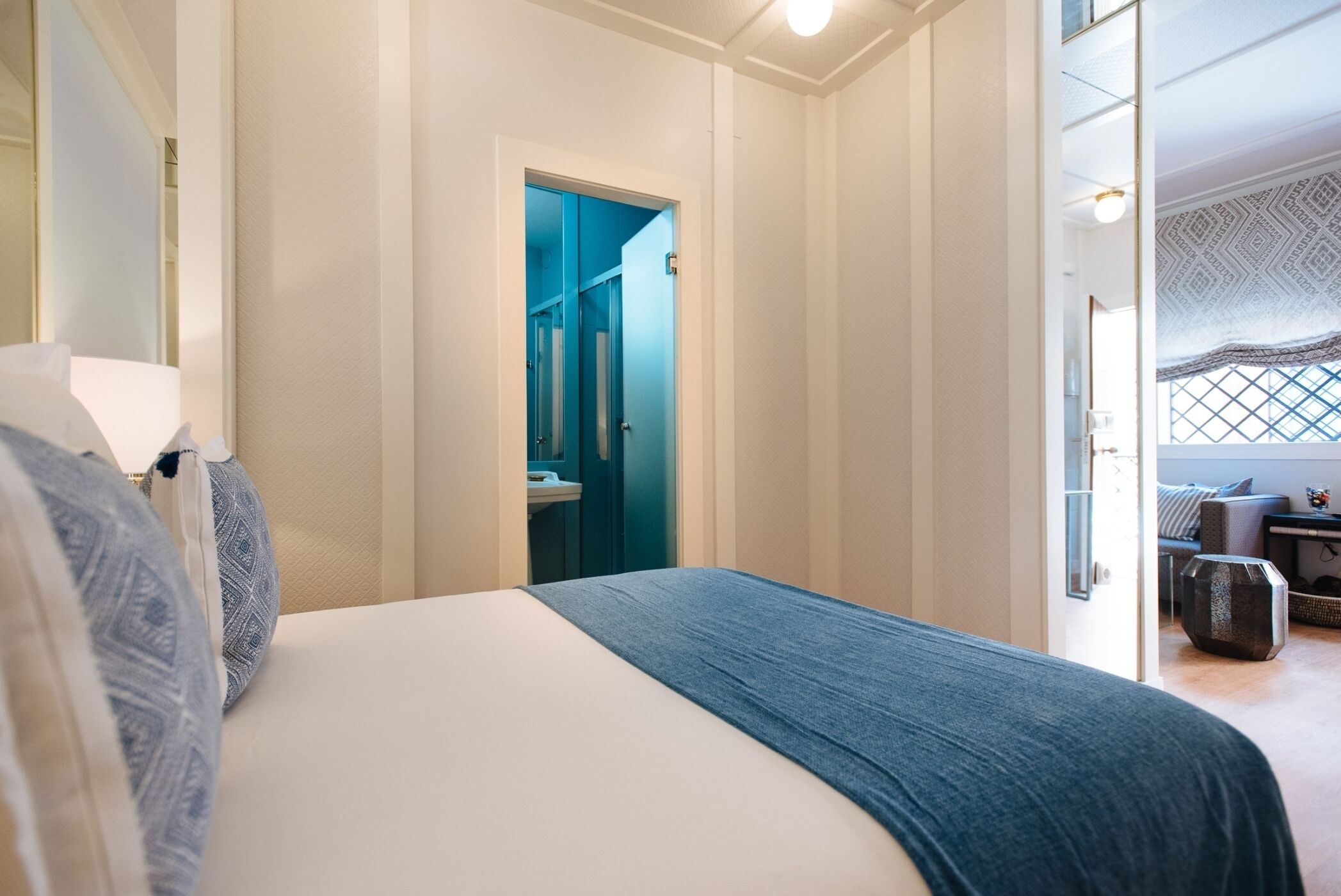 Une chambre à coucher avec un lit, une salle de bain visible à travers une porte ouverte, et un coin salon avec une table et des chaises.