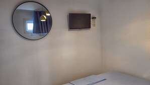 A bedroom with a bed, a round mirror, a flat-screen TV, and pendant lights.