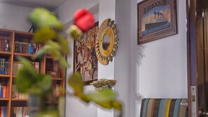 A living room with a wooden bookshelf, a blue sofa, a striped cushion, a framed picture of the Titanic, and a mirror with a sun design.