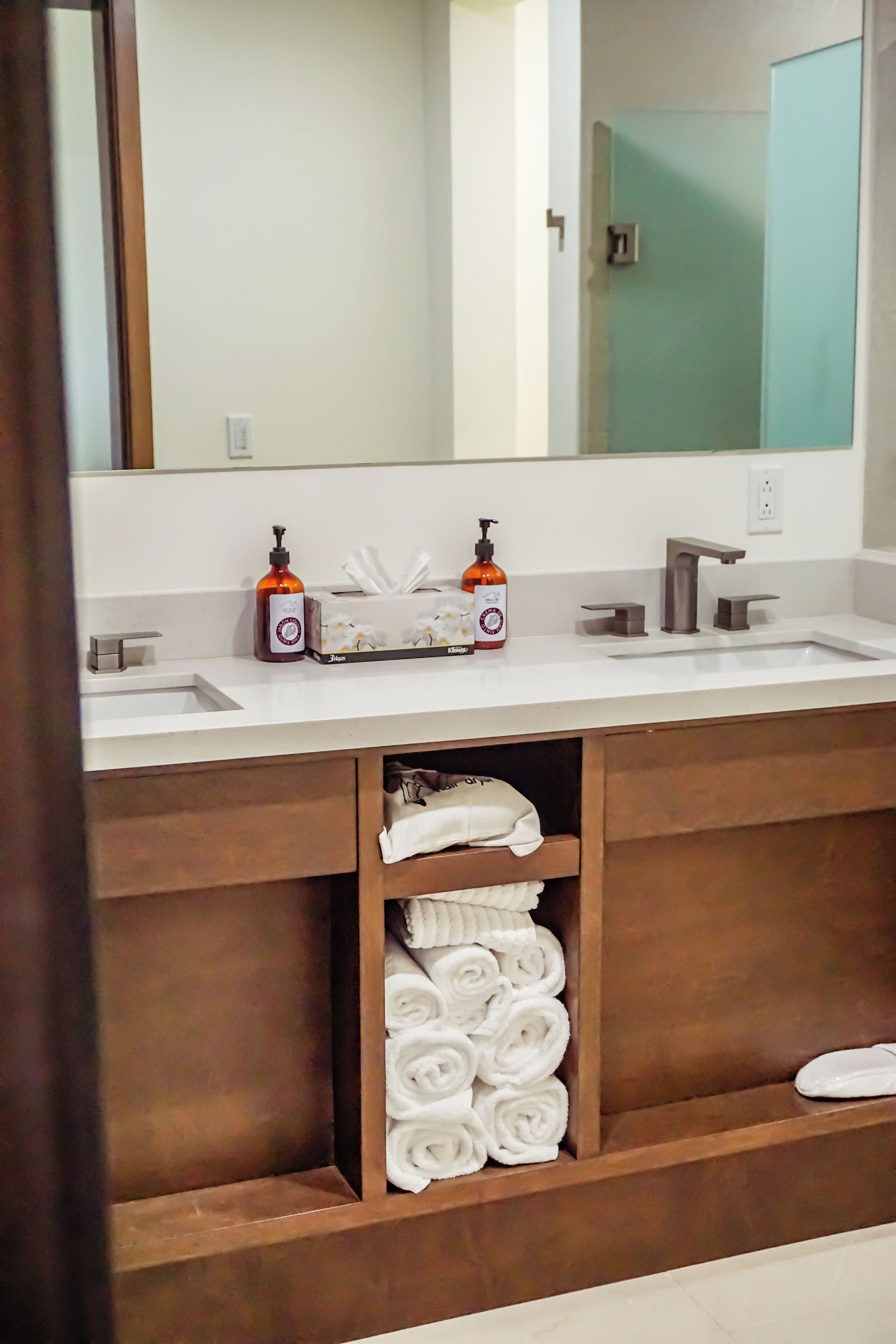 A bathroom with two sinks, a large mirror, and a towel rack with neatly folded towels.