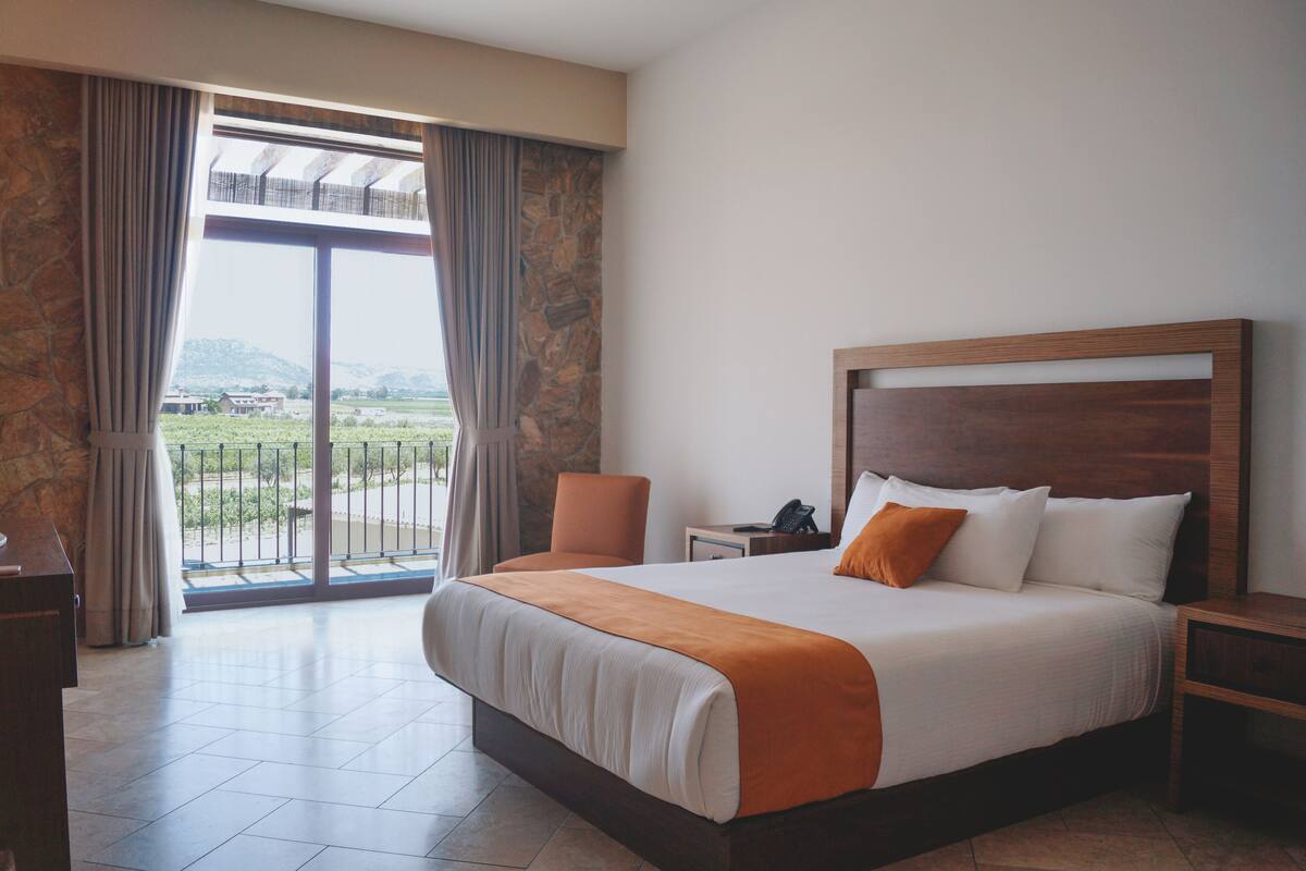 Habitación de hotel con una cama grande, una silla, una mesita de noche y vistas al exterior.
