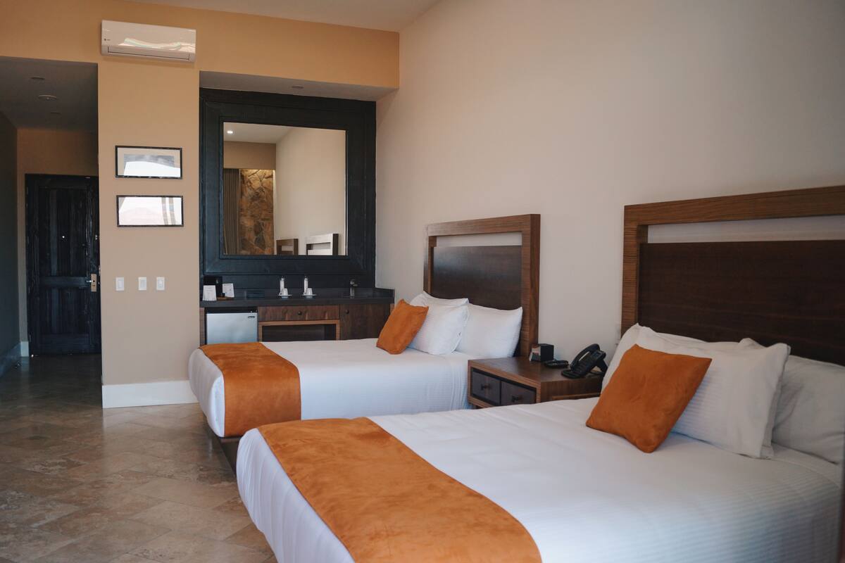 Habitación de hotel con dos camas, un espejo grande, un cabecero de madera y un escritorio pequeño con teléfono.