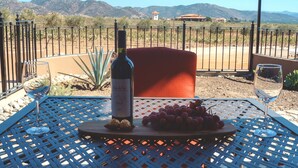 Una mesa con una botella de vino, uvas y dos copas, frente a un paisaje montañoso.