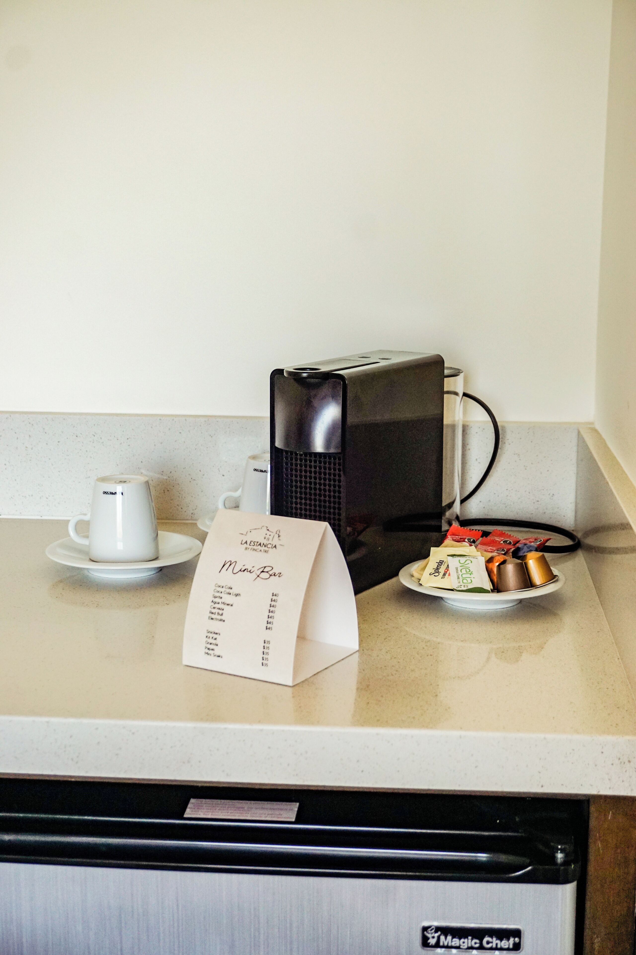 Un comptoir de cuisine avec une machine à café, un panneau indiquant la présence d’un bar, et une assiette de collations.