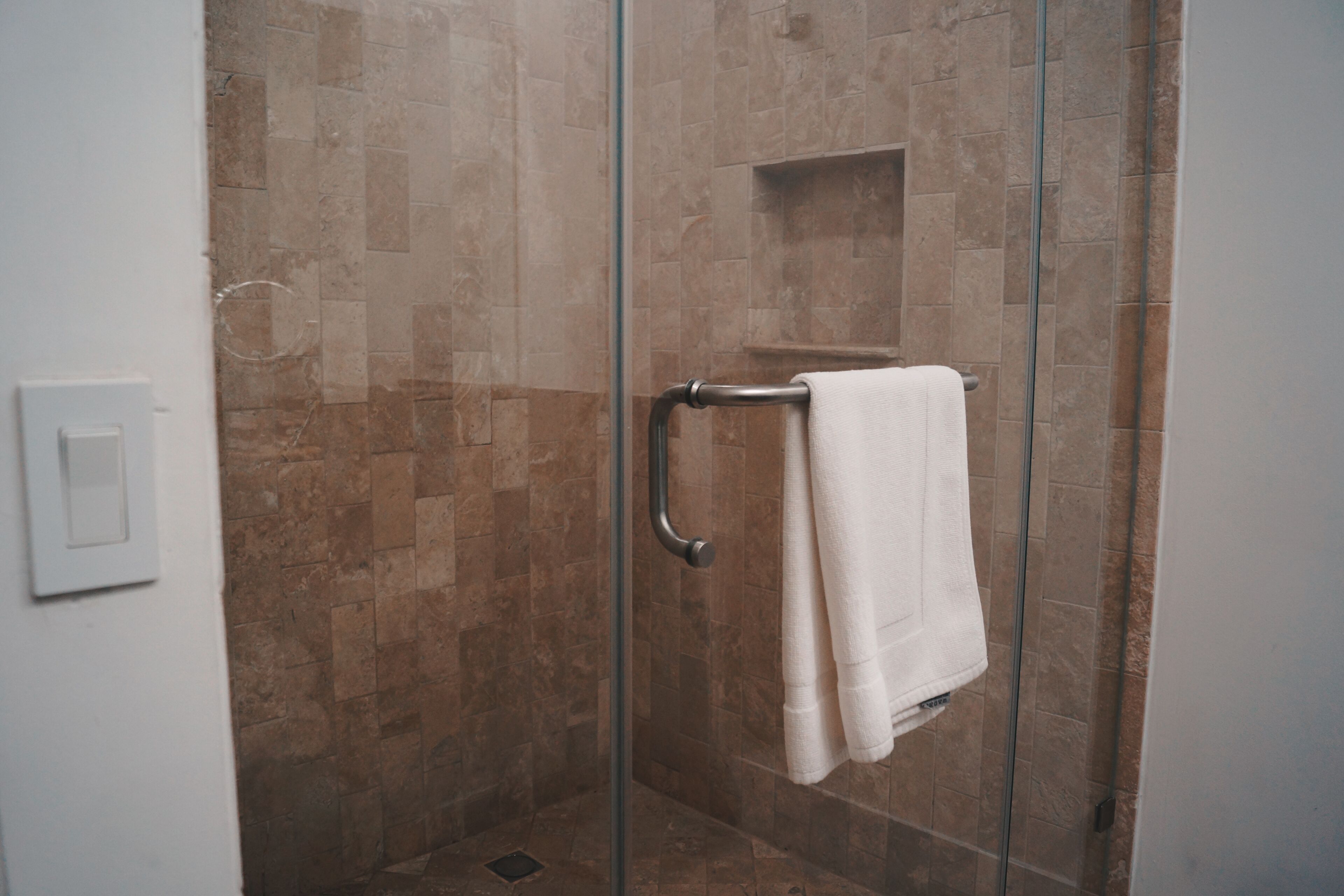 A glass-enclosed shower with a white towel hanging on a metal towel rack.