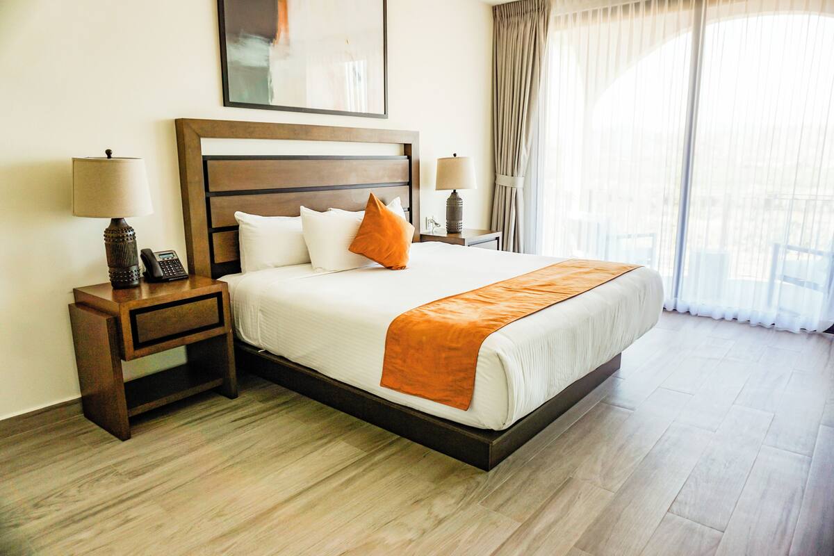 Habitación de hotel con una cama grande, dos mesitas de noche, un tocador, un espejo y una ventana con cortinas.