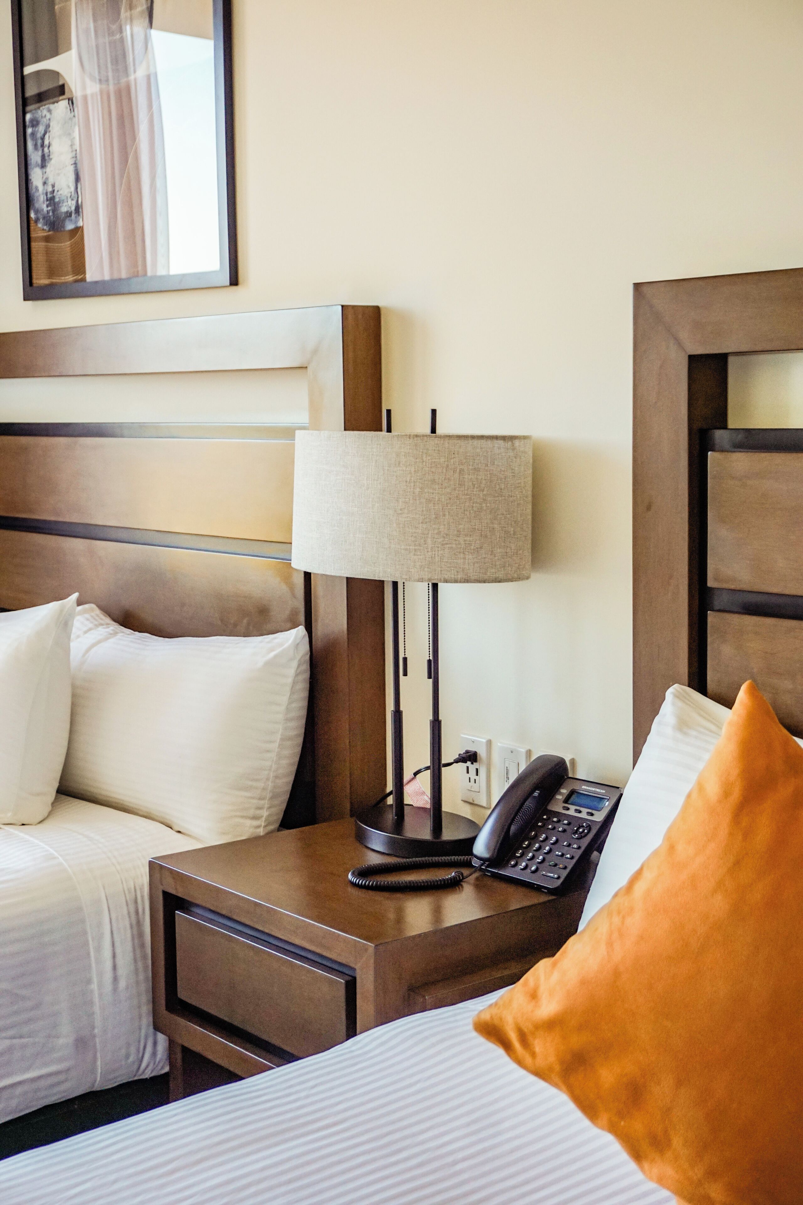A hotel room with a bed, a nightstand with a lamp, a phone, and a framed picture on the wall.
