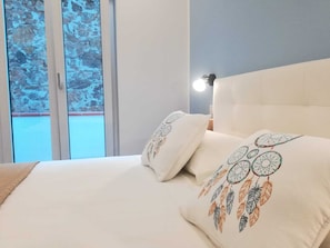Relax in a serene space with a large bed, dreamcatcher-patterned pillows, and a stunning view of the surrounding rocky landscape.