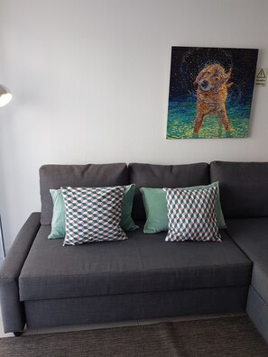 A grey sofa with patterned cushions and a painting of a dog on the wall.