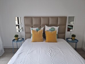 Un lit avec une tête de lit capitonnée, deux tables de chevet avec des lampes et des coussins décoratifs.