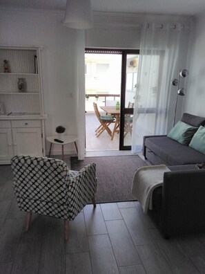 Uma sala de estar moderna com um sofá, uma poltrona estampada e um espaço de jantar com mesa e cadeiras.