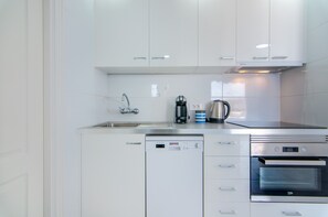 A modern kitchen with white cabinetry, a stainless steel sink, a coffee maker, a kettle, and a built-in oven. - La Estrella 1A020 con vistas panorámicas al mar (Los Cristianos)