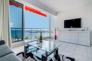 Een moderne woonkamer met een glazen salontafel, een flatscreen televisie en uitzicht op de zee.