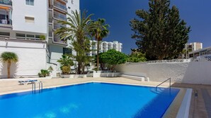 A swimming pool with a clear blue water, surrounded by white buildings and palm trees. - La Estrella 1A020 con vistas panorámicas al mar (Los Cristianos)