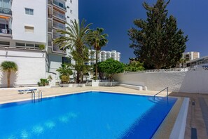 A swimming pool with a clear blue water, surrounded by white buildings and palm trees. - La Estrella 1A020 con vistas panorámicas al mar (Los Cristianos)
