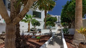 A courtyard with palm trees, a white building, and a pathway. - La Estrella 1A020 con vistas panorámicas al mar (Los Cristianos)