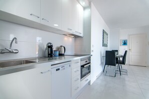 A modern kitchen with white cabinetry, a built-in dishwasher, and a coffee maker.