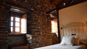 A rustic room with a stone wall, wooden beams, a bed with white bedding, and a wooden headboard.