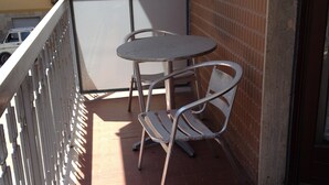 En balkon med et metalbord og to stole, et hvidt gelænder og en murstensvæg.
