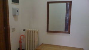 Et lille værelse med en radiator, et træskrivebord og et spejl på væggen.
