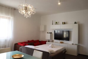 Une chambre d’hôtel moderne équipée d’un lit, d’un canapé, d’une table à manger, d’un téléviseur et d’un lustre.
