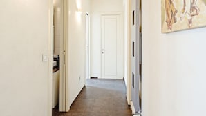 Un pasillo con una puerta blanca al final, suelo de baldosas y una obra de arte colgada en la pared.