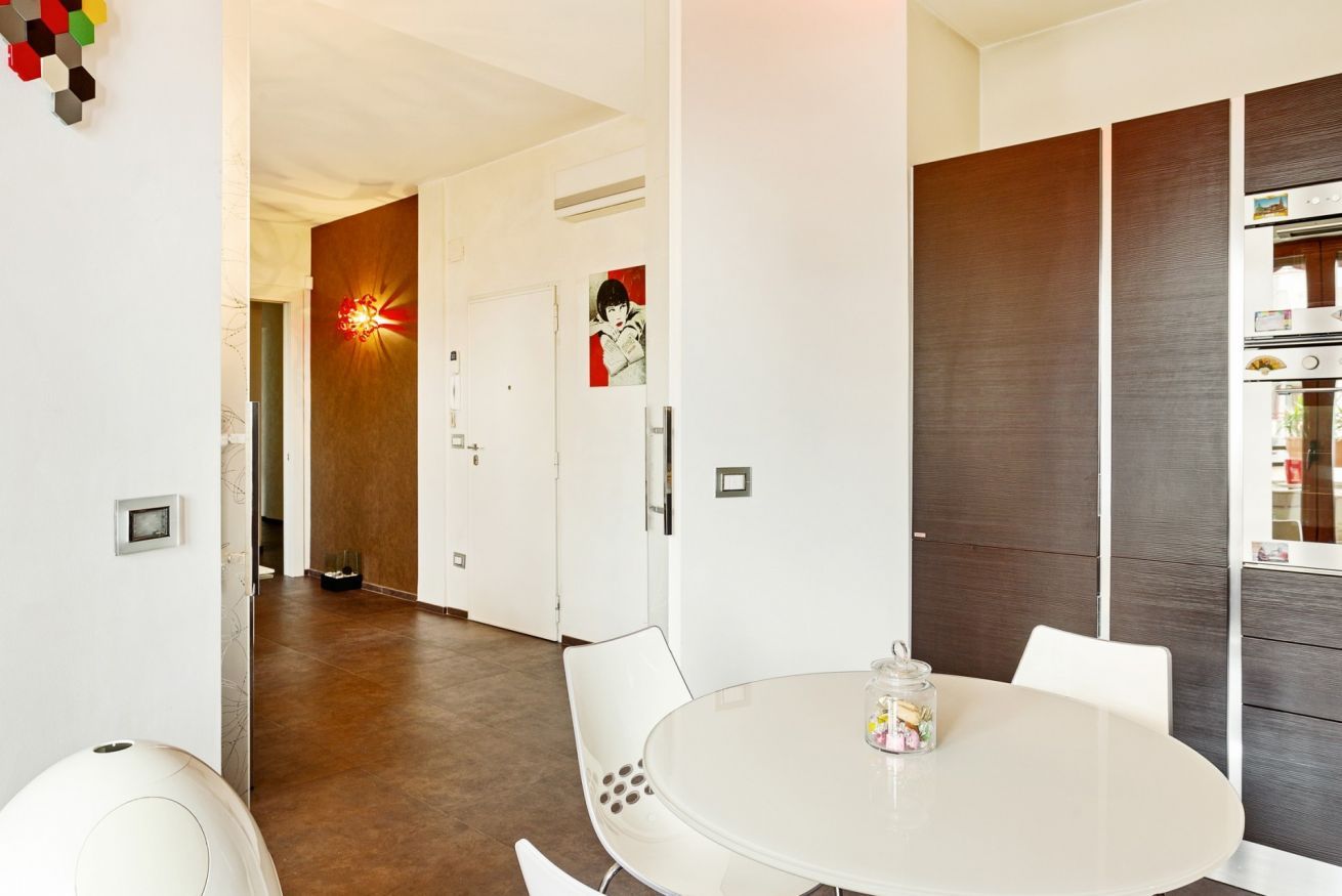 Ein modernes Interieur mit einem runden Esstisch, weißen Stühlen, einer Holzwand und einem Flur, der in einen weiteren Raum führt.