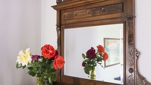 Un aparador de madera con un espejo encima, que refleja un jarrón con flores y una pequeña planta en maceta.