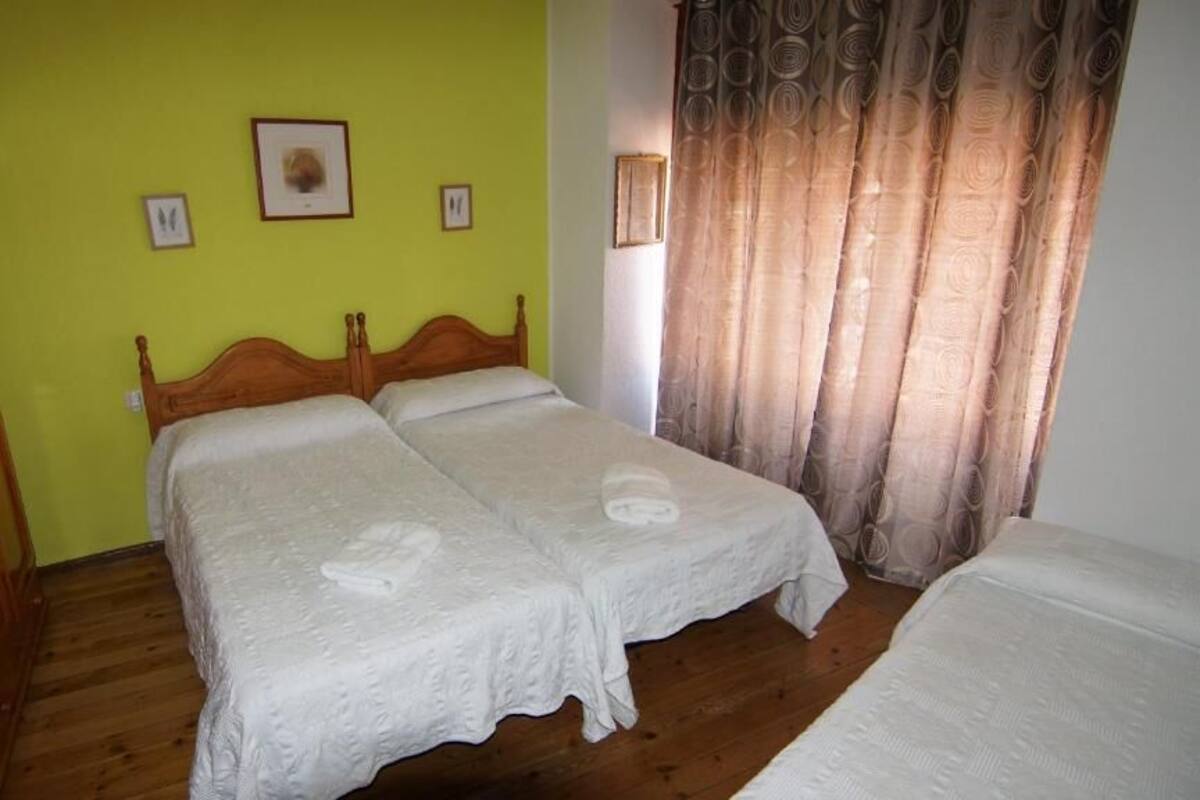 Una stanza con due letti singoli, un armadio in legno e una finestra con tende.