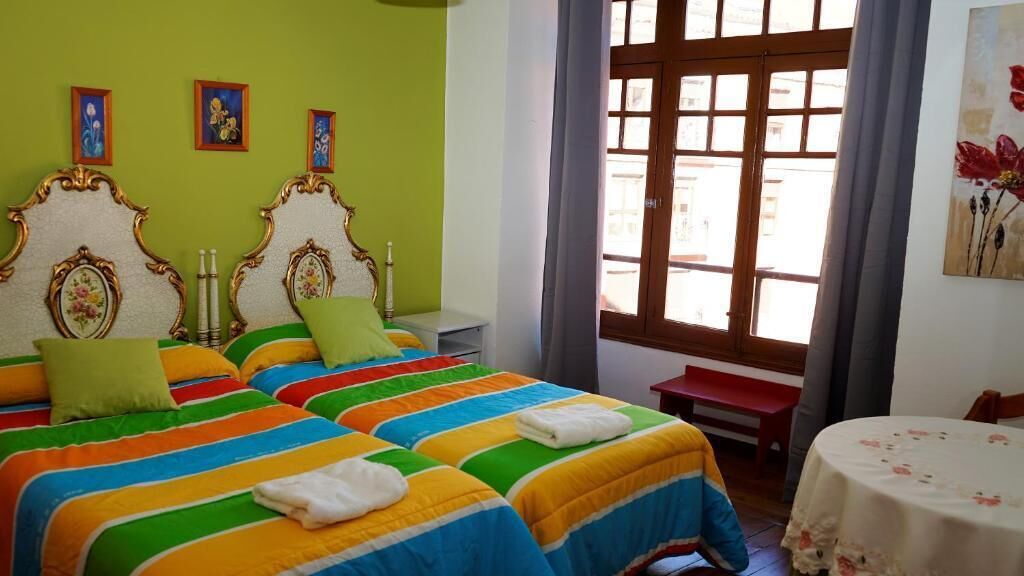 A room with two beds, a small table, and a window with curtains.