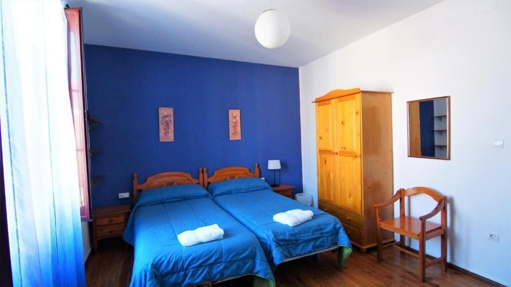 Une chambre avec deux lits, une armoire en bois, une chaise et un miroir au mur.