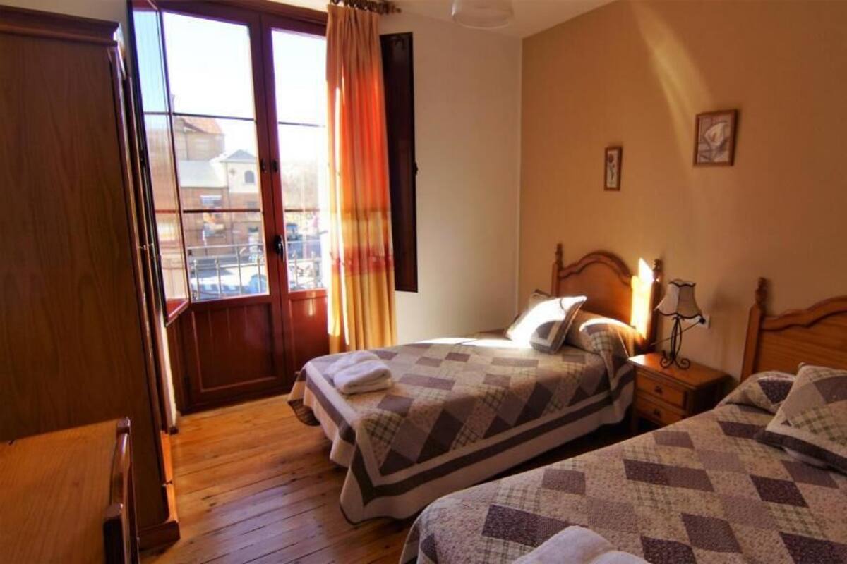 Una camera da letto con due letti, pavimento in legno, finestra con tende e vista all'esterno.