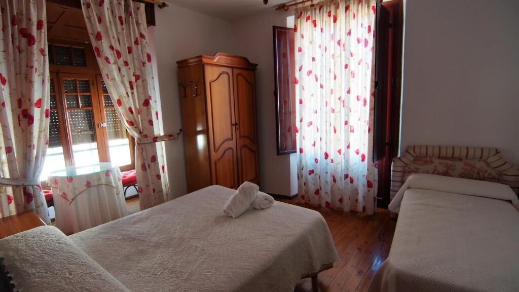 Un dormitorio con dos camas, un armario y una ventana con cortinas florales.