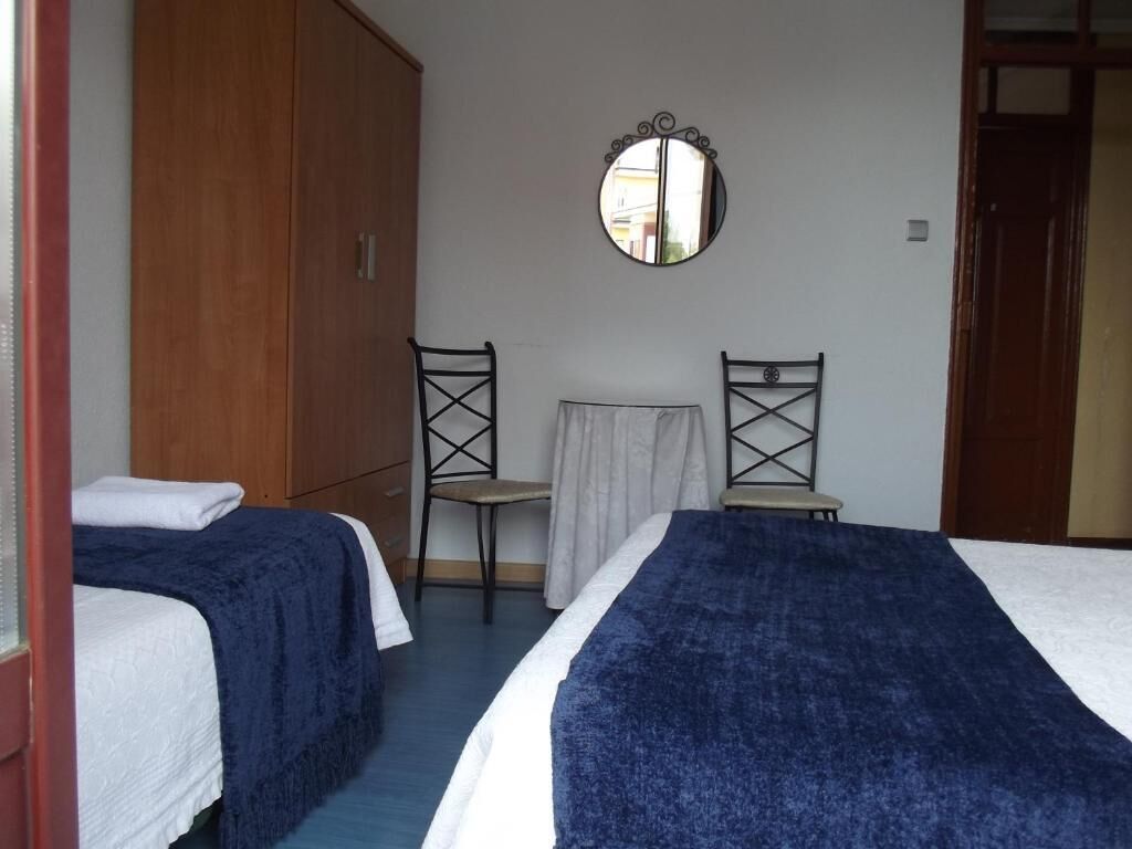 A bedroom with two beds, a wooden wardrobe, a mirror, and a small table with a chair.