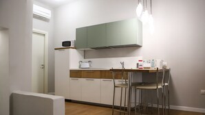 Una cucina compatta con forno a microonde, macchina del caffè e un piccolo spazio pranzo con sedie in metallo.
