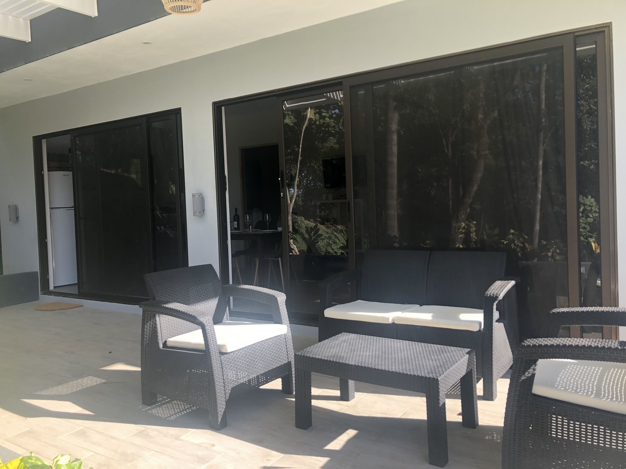 An outdoor patio with wicker furniture, a sliding glass door, and a view of the surrounding greenery.