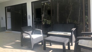 An outdoor patio with wicker furniture, a sliding glass door, and a view of the surrounding greenery. - Condominios Las Navieras (Tamarindo)
