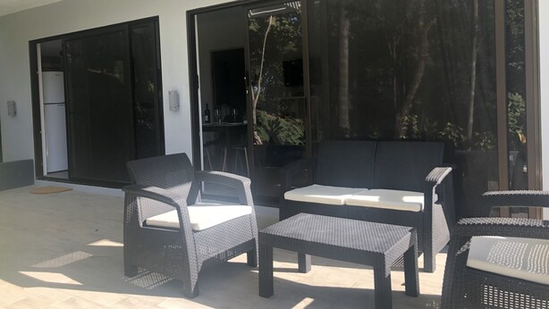An outdoor patio with wicker furniture, a sliding glass door, and a view of the surrounding greenery. - Condominios Las Navieras (Tamarindo)
