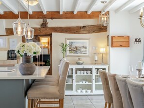 Un espace repas doté d’un plafond en bois, de luminaires suspendus, d’une table blanche et de chaises rembourrées.