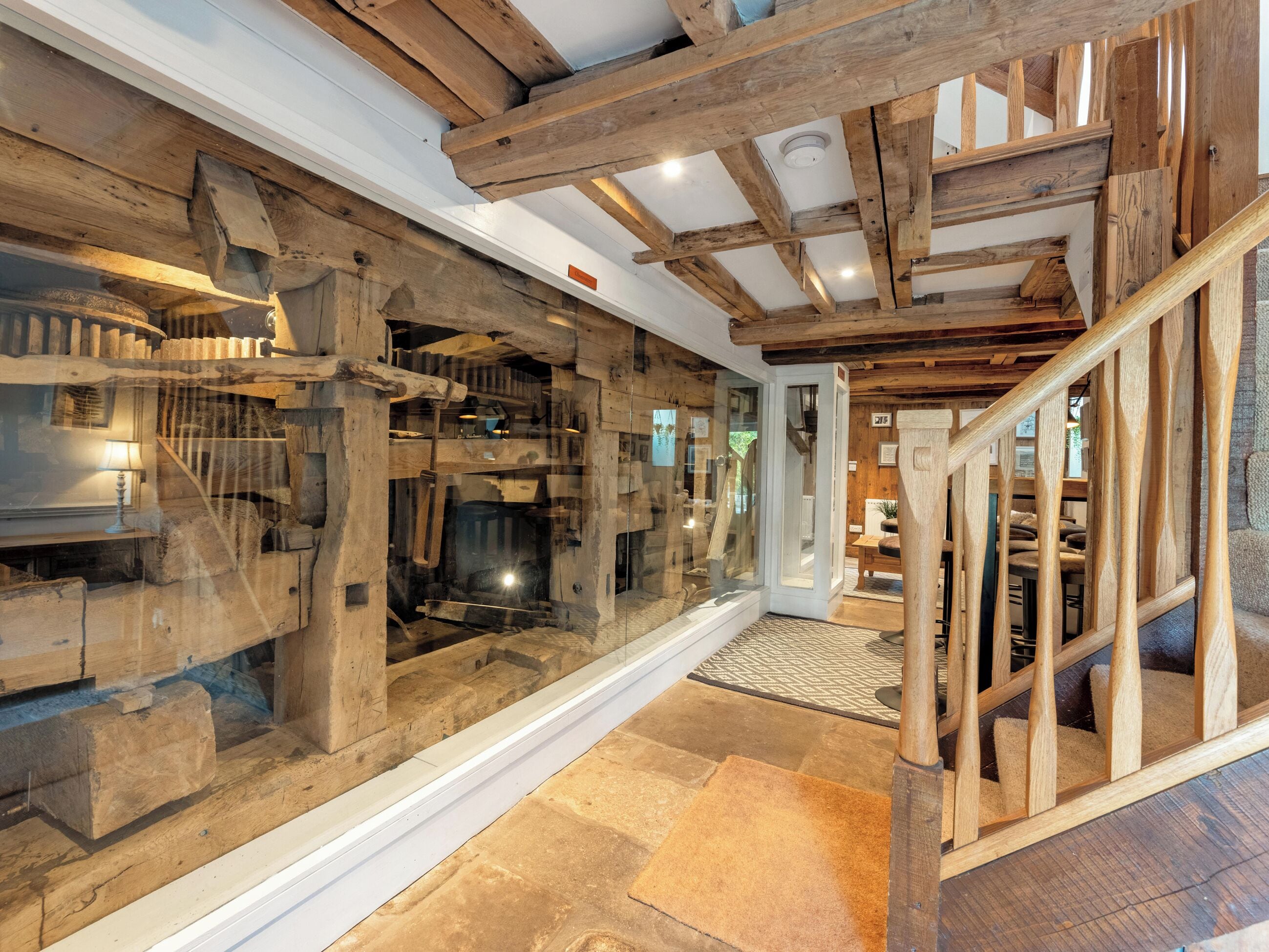A rustic interior with exposed wooden beams, a glass display case, and a wooden staircase.