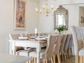 Un comedor con una mesa blanca dispuesta para seis comensales, una araña y un espejo en la pared.