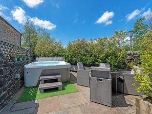 Un jacuzzi, mobiliario de exterior y un muro de piedra en un patio trasero.