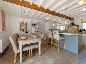 A dining area with a wooden table set for six, a kitchen with a central island, and a ceiling with exposed beams. - 7 bedroom accommodation in Bradbourne, near Ashbourne (Bradbourne, near Ashbourne)