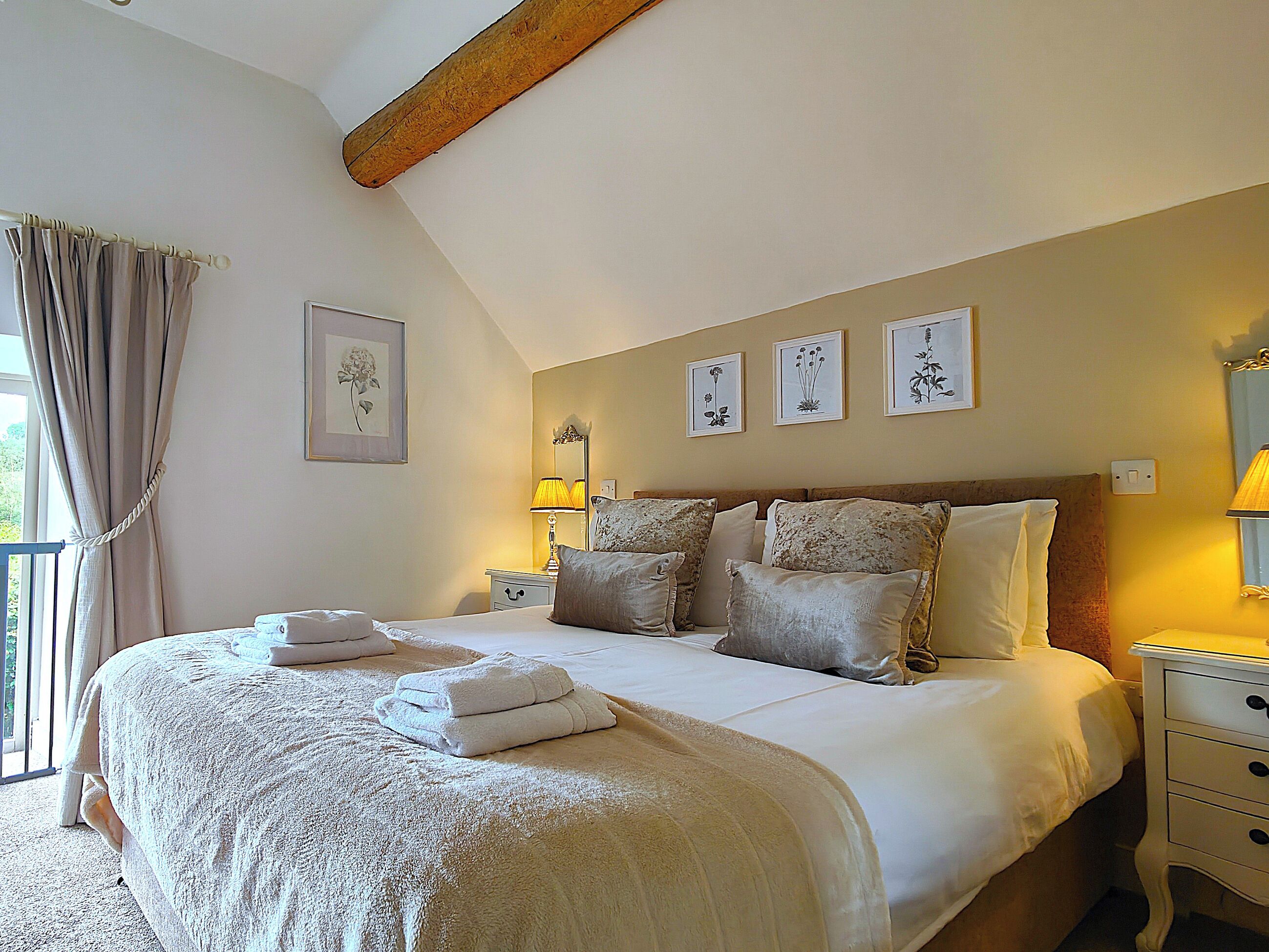 A bedroom with a large bed, bedside tables, a lamp, and framed botanical prints on the wall.