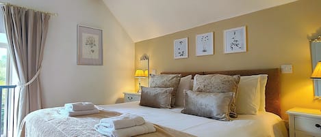 A bedroom with a large bed, bedside tables, a lamp, and framed botanical prints on the wall.