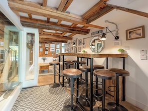 Un espace bar avec des poutres en bois, un comptoir, des tabourets, des tableaux encadrés au mur et une enseigne indiquant « Bar à champagne ».